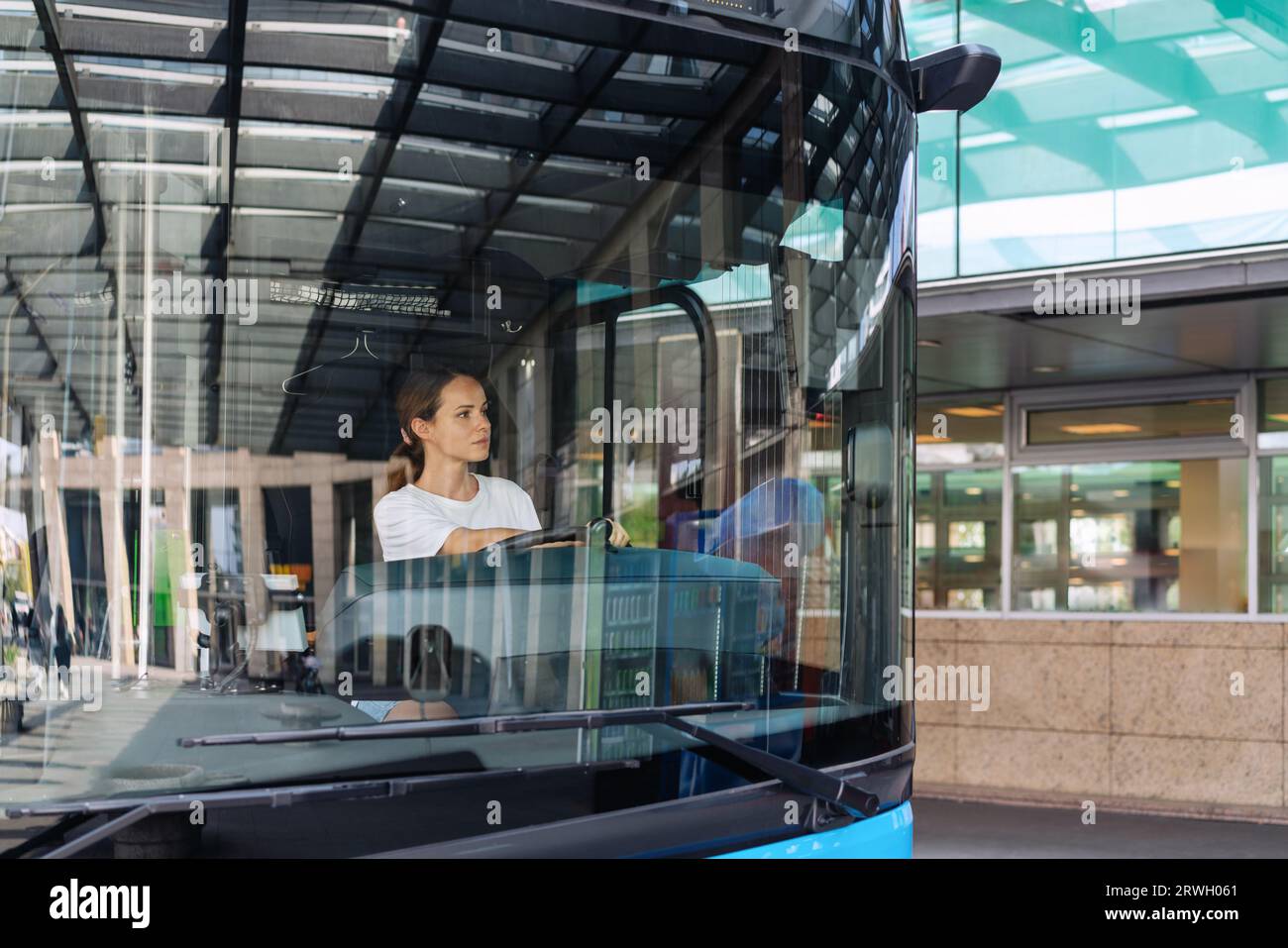 Junge Frau, die einen Shuttlebus an einer Vorstadtbusstation fährt, weibliche Shuttlebusfahrerin Beruf und Beschäftigung. Stockfoto