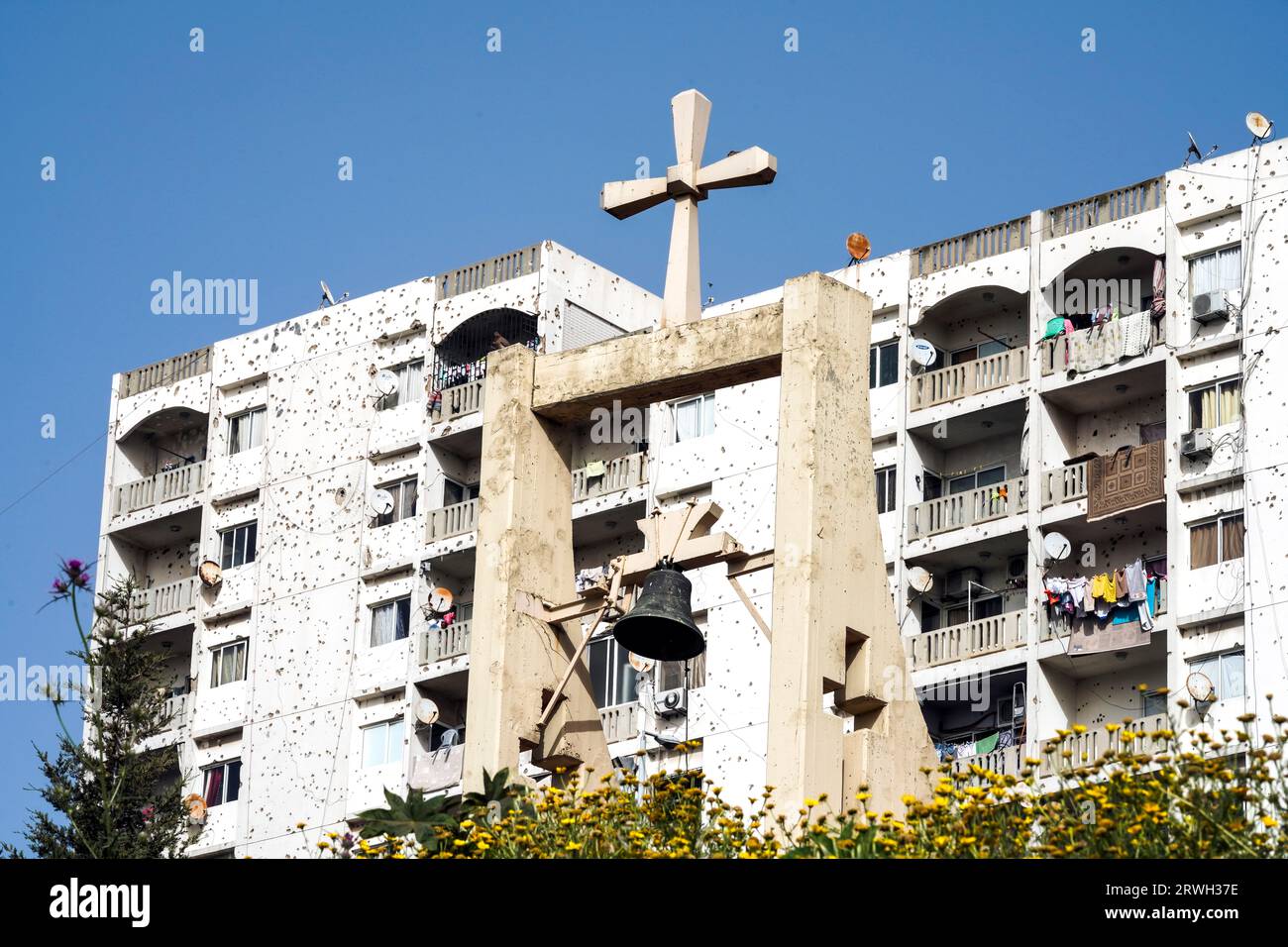 Glockenturm mit einem Kreuz über einer Kirche vor Wohngebäuden, die mit Einschusslöchern in Tripolis, Libanon, bedeckt sind Stockfoto