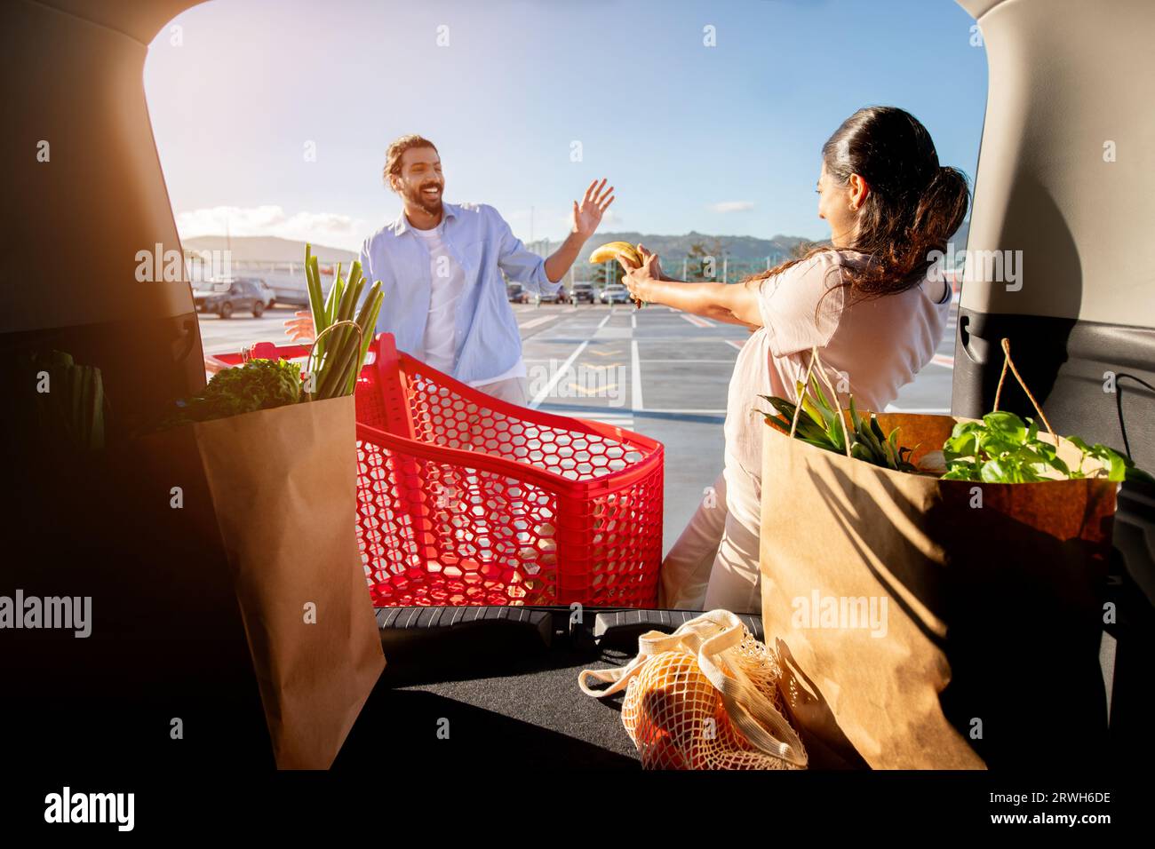 Fröhliches lateinisches Paar, das Spaß beim Laden von Einkäufen im Auto hat, Blick vom Fahrzeuginnenraum Stockfoto