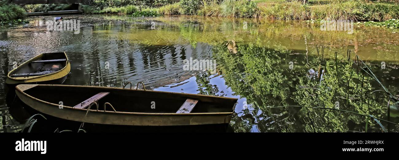2 alte hölzerne Ruderboote liegen auf dem Wasser am Ufer eines ruhigen idyllischen Sees. Bäume aus grünem Sommerwald spiegeln sich auf glatter Oberfläche wider. Ruhig ruhig und entspannend Stockfoto
