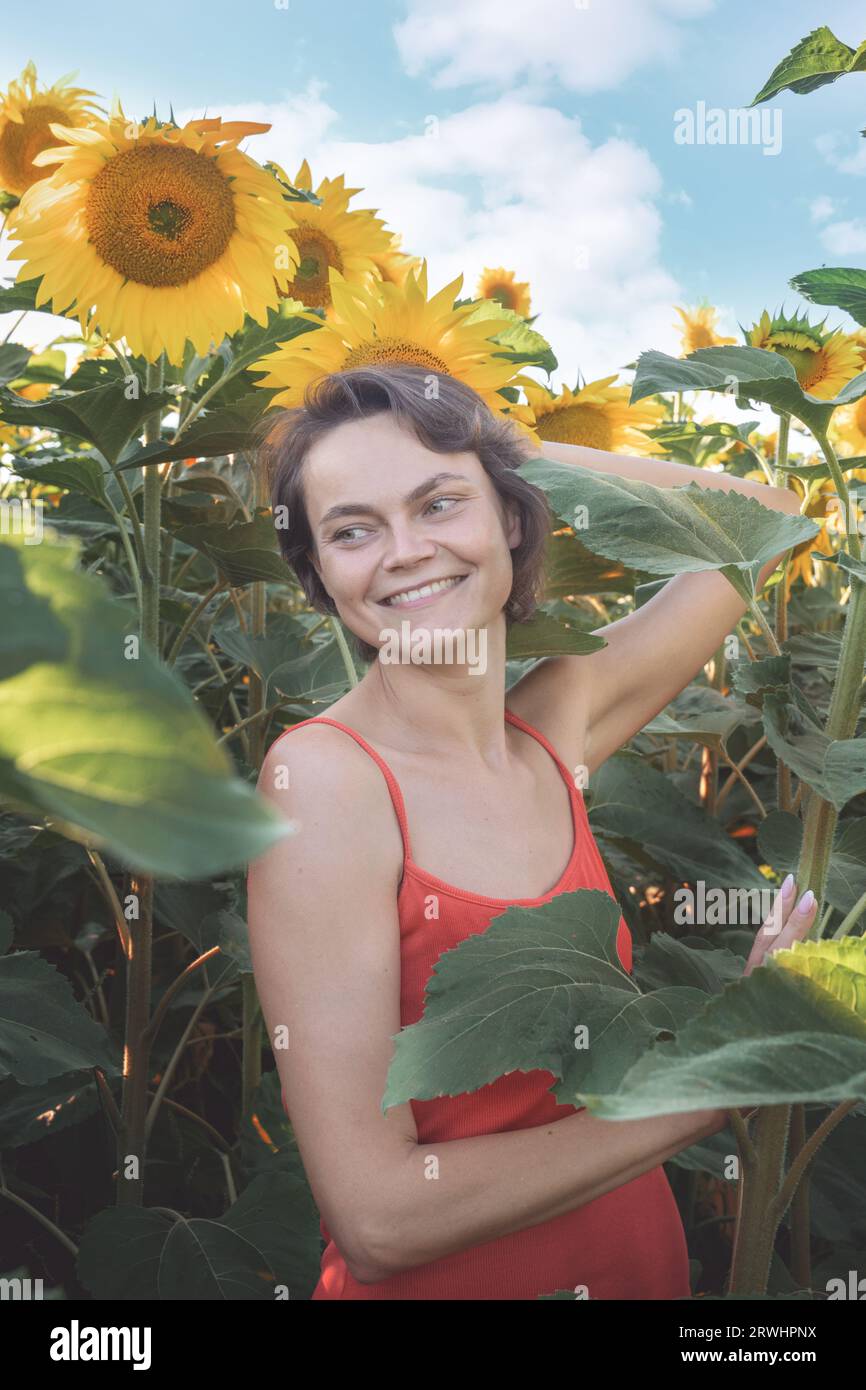 Frau im Sonnenblumenfeld: Glückliches Mädchen mit Strohhut, das sich bei Sonnenuntergang auf einem riesigen Feld mit Sonnenblumen posiert, genießen Sie es, Fotos im Freien zu machen, um Erinnerungen zu sammeln. Sommer Stockfoto