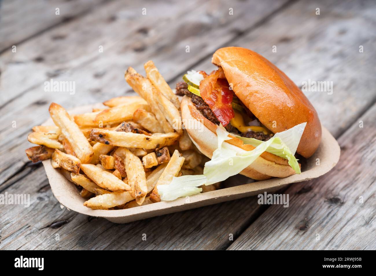 Ein Burger mit Speck zum Mitnehmen und frischen Pommes frites. Wird in einem kompostierbaren Papierfach serviert. Stockfoto