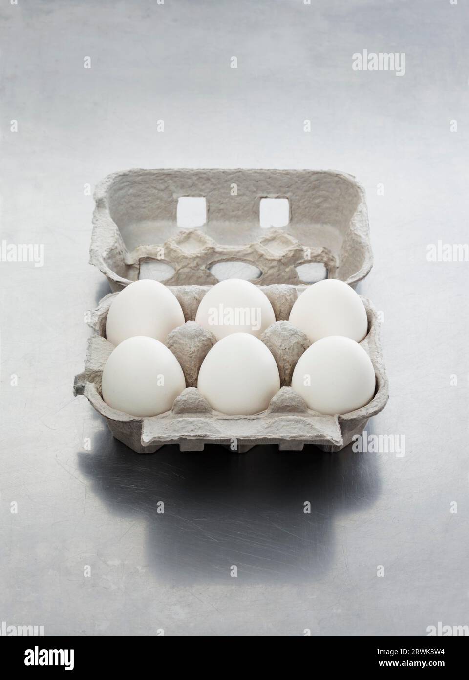 Ein Eierkarton mit sechs weißen Eiern auf metallischer Oberfläche Stockfoto