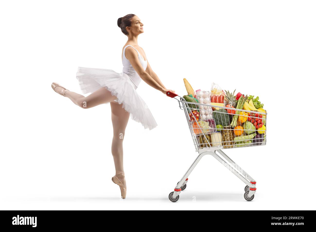 Profilaufnahme in voller Länge einer Ballerina, die tanzt und einen Einkaufswagen schiebt, mit Lebensmittelprodukten, die auf weißem Hintergrund isoliert sind Stockfoto