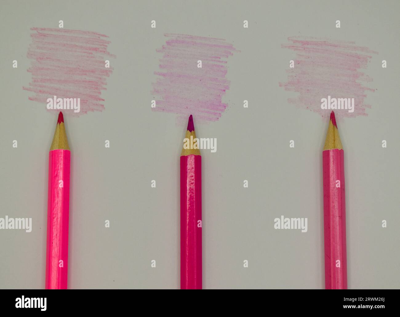 Drei rosa Buntstifte, die neben ihren jeweiligen Farbtönen auf weiße Karten gelegt werden. Stockfoto
