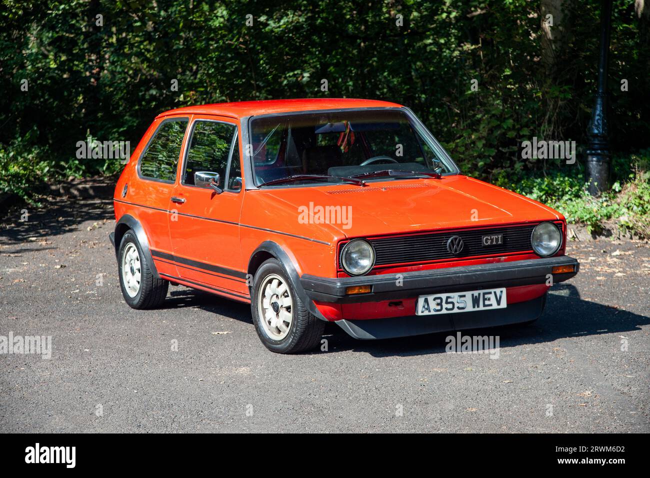 Der verwitterte Volkswagen Golf GTi parkte an einem heißen Sommertag auf einem Parkplatz mit Bäumen und Büschen dahinter Stockfoto