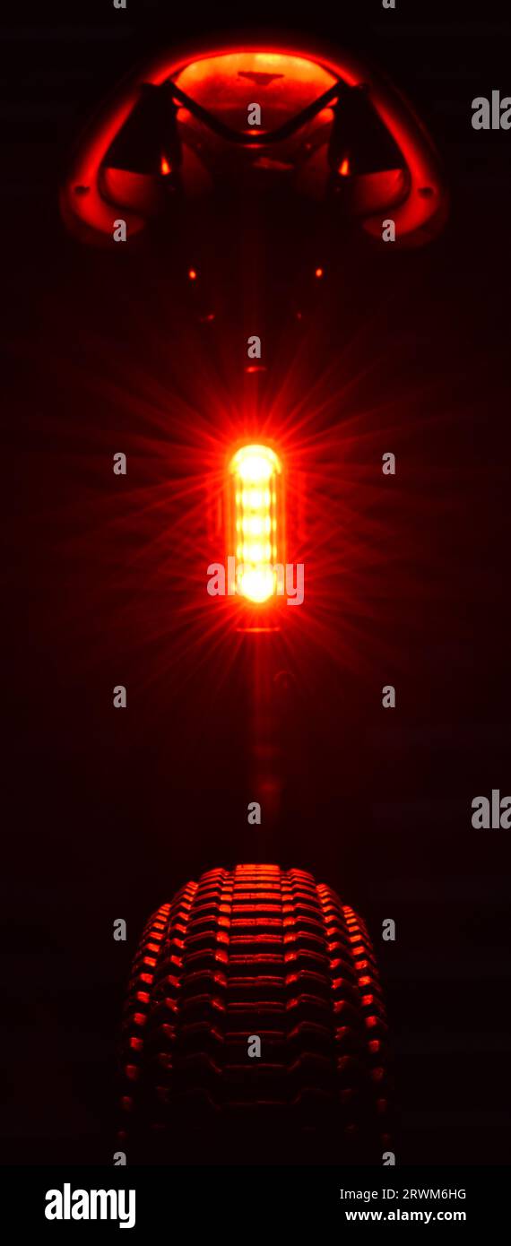 Die leuchtend rote hintere LED-Leuchte eines Mountainbikes beleuchtet die Unterseite des Satteles und die Oberseite des Hinterreifens und hebt das Profilprofil hervor. Stockfoto