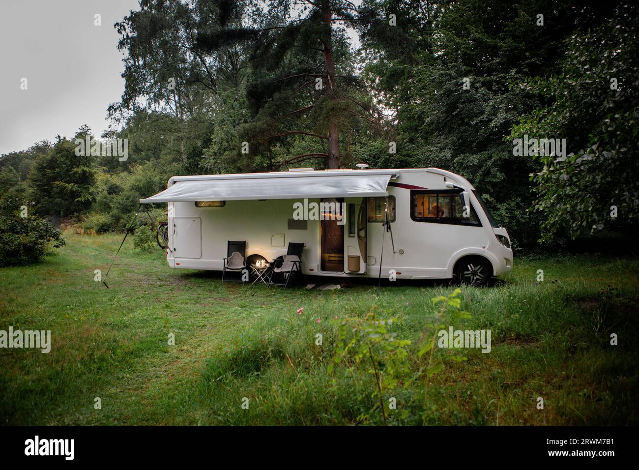 Ruhige Szene im Herzen der Natur, wo ein Wohnmobil auf einer Waldlichtung geparkt ist. Draußen stehen Stühle auf, und die Markise ist erweitert, kreati Stockfoto