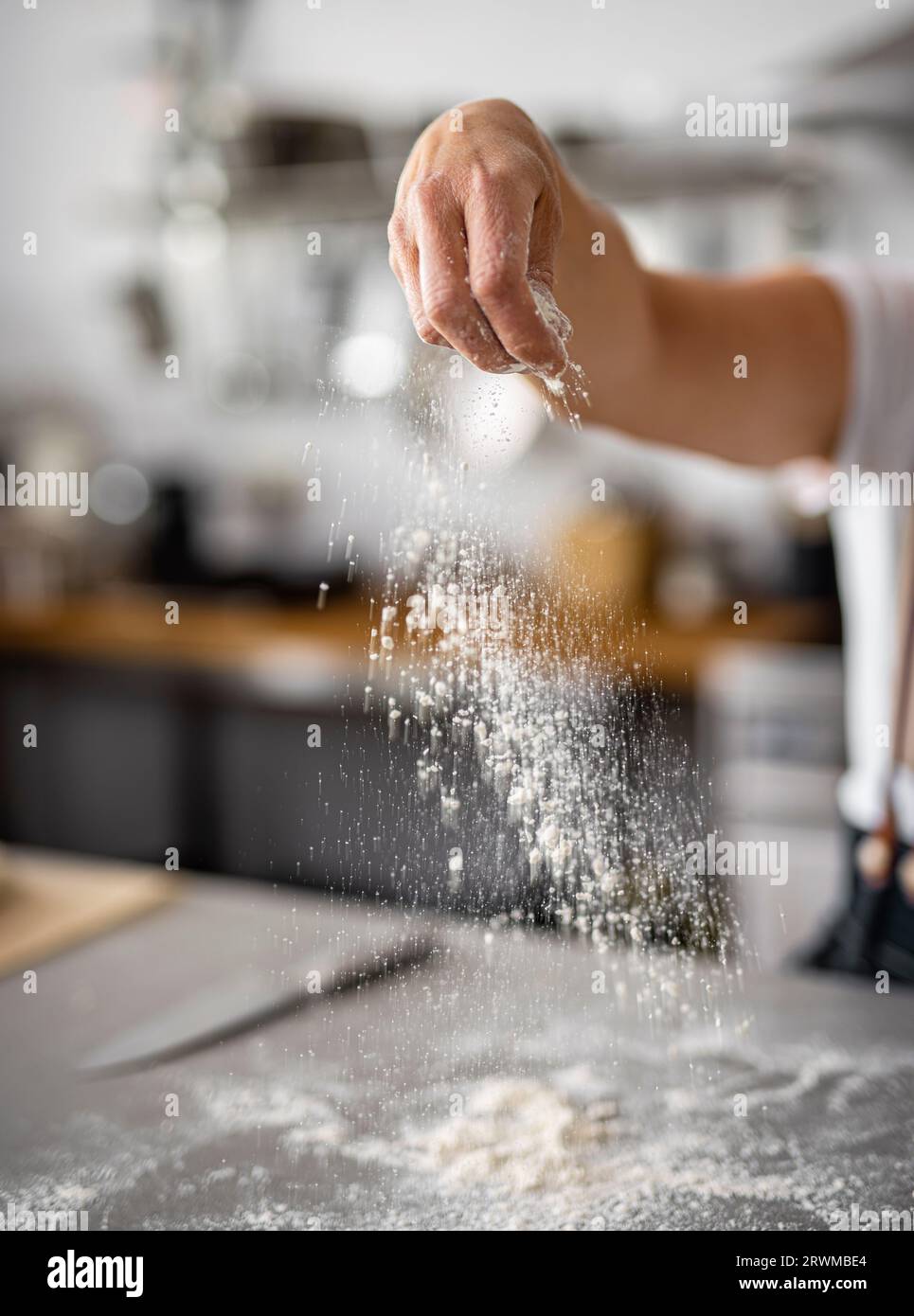 Eine Frau wird beim Backen gesehen, während ihre Hand anmutig weißes Mehl auf eine Backfläche gießt. Stockfoto