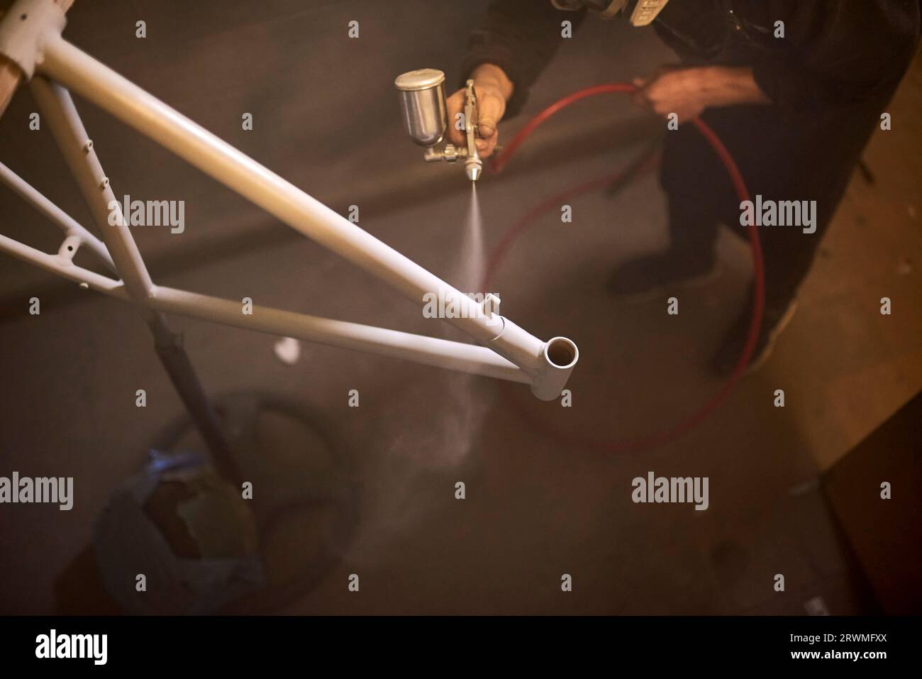 Nicht erkennbarer Mensch sprüht in seiner Werkstatt einen Fahrradrahmen auf. Komposition von Ansichten mit hohem Winkel und Kopierraum. Stockfoto