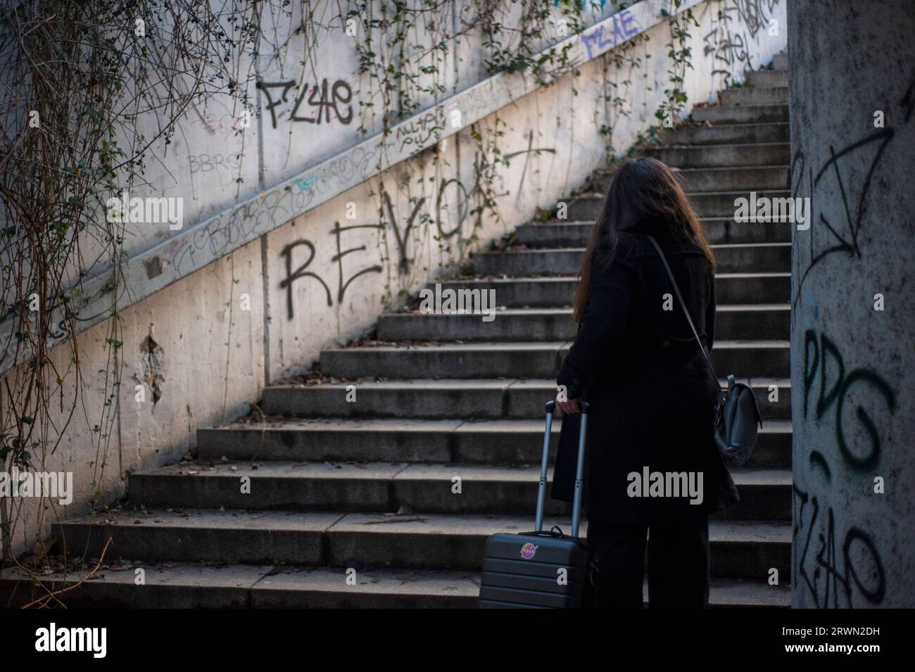 Frau mit Koffer, die aus einer Unterführung mit Graffiti unter Weinstöcken die Treppe rauf geht Stockfoto