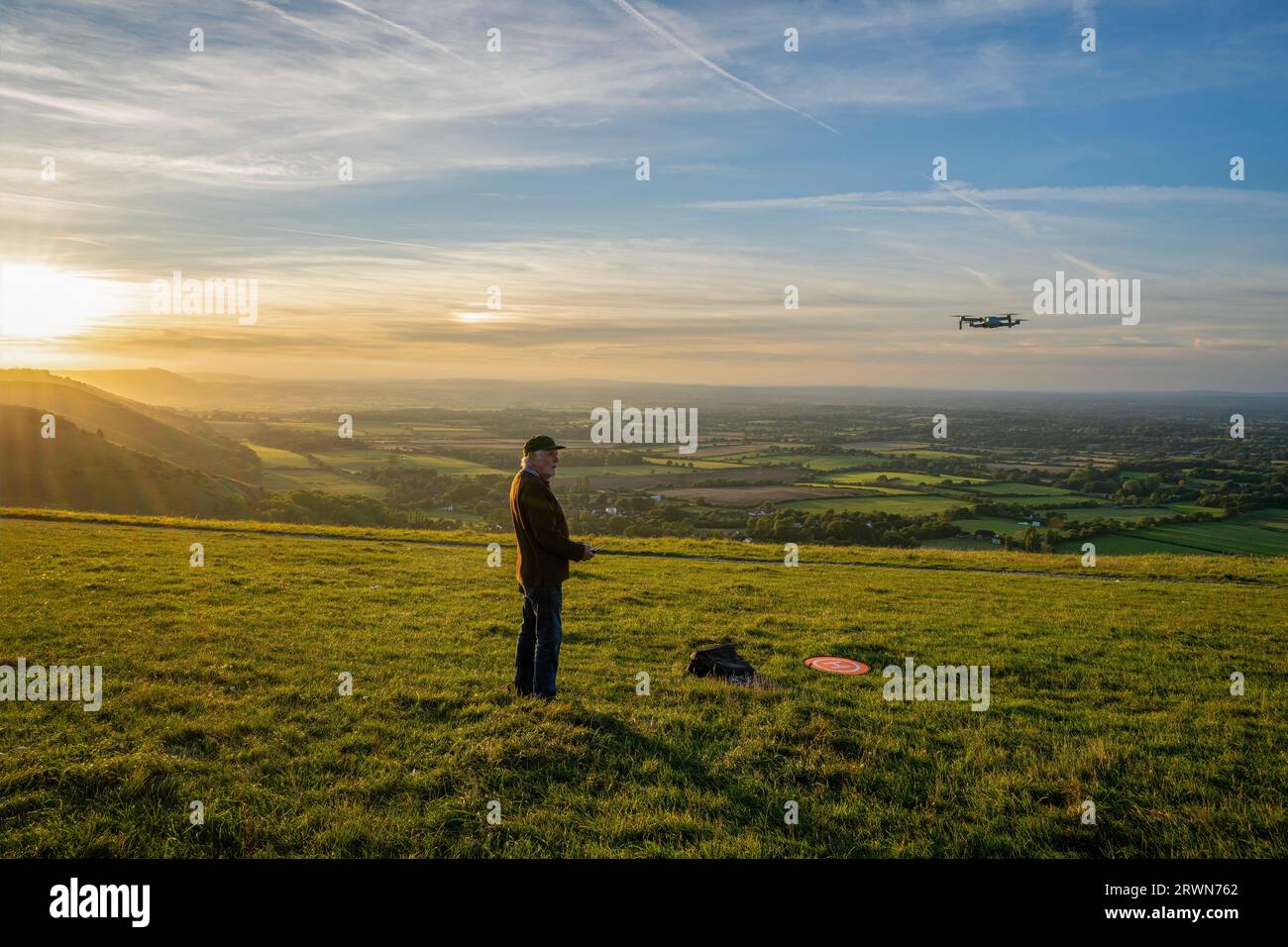 Kaukasischer Mann, der eine Drohne per Fernbedienung über die South Downs Landschaft während des Sonnenuntergangs am Devil's Dyke bei Brighton in West Sussex, England, betreibt Stockfoto