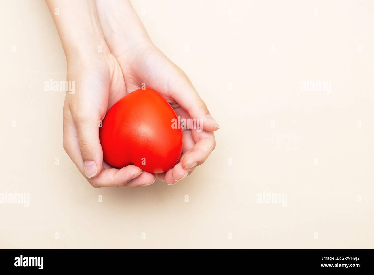 Kinderhände halten ein rotes Herz als Symbol für Pflege, Liebe, Unterstützung und Schutz isoliert auf beigem Hintergrund. Kindergesundheitskonzept. Stockfoto