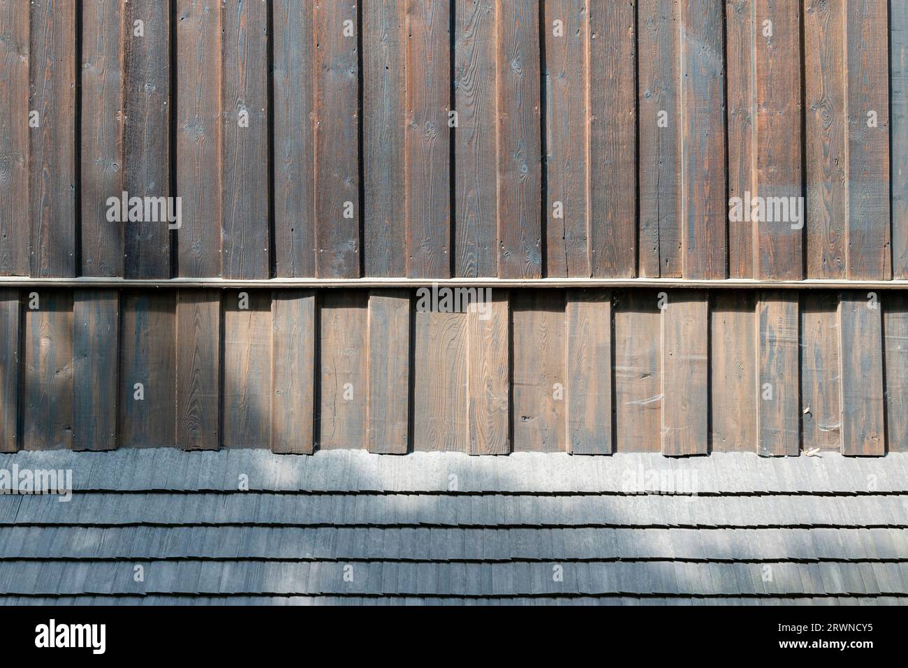 Detail der Fassade einer alten Holzkirche. Holzbretter und Holzschindeln. Der Schatten der Bäume wird auf die Fassaden geworfen Stockfoto