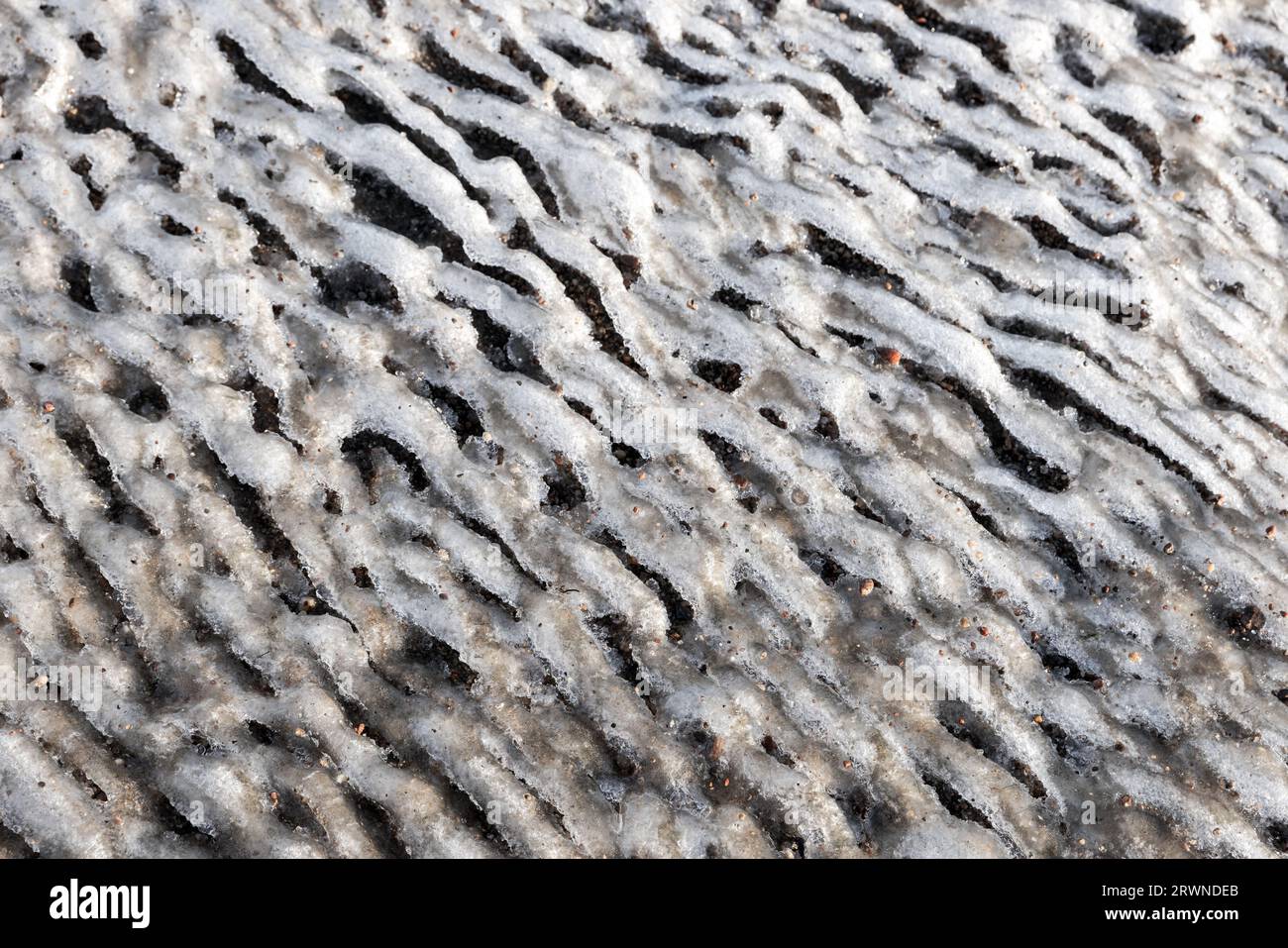 Abstraktes Wellenmuster aus schmelzendem Küsteneis, gemischt mit Sand. Natürliches Hintergrundfoto Stockfoto