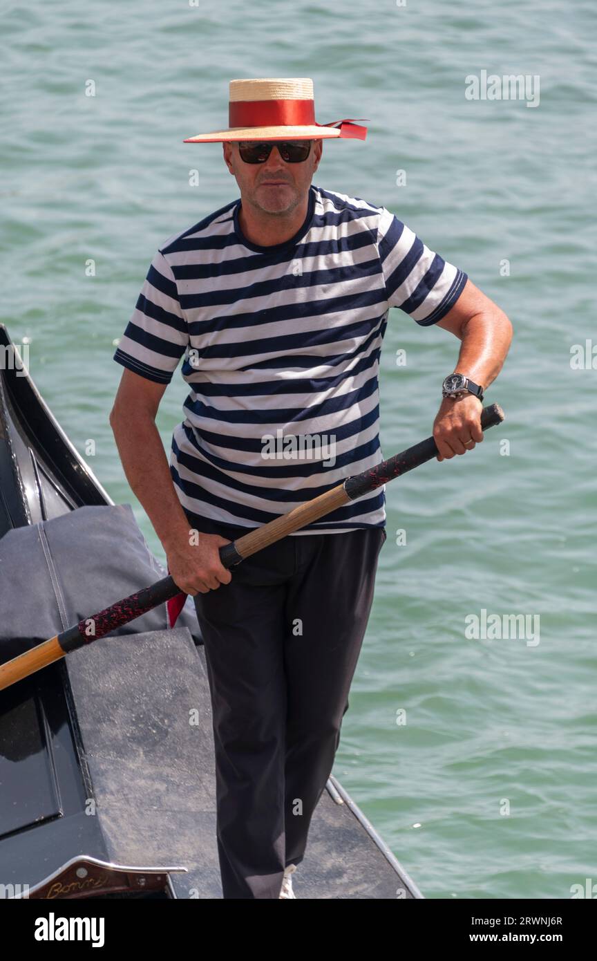 Ein Gondolier mit seinem bekannten schwarz-weiß gestreiften Hemd und Bootsfahrer ist ein Ruderer, der eine Gondel mit einem langen Ruder steuert und Touristen für eine kurze Tour nimmt Stockfoto