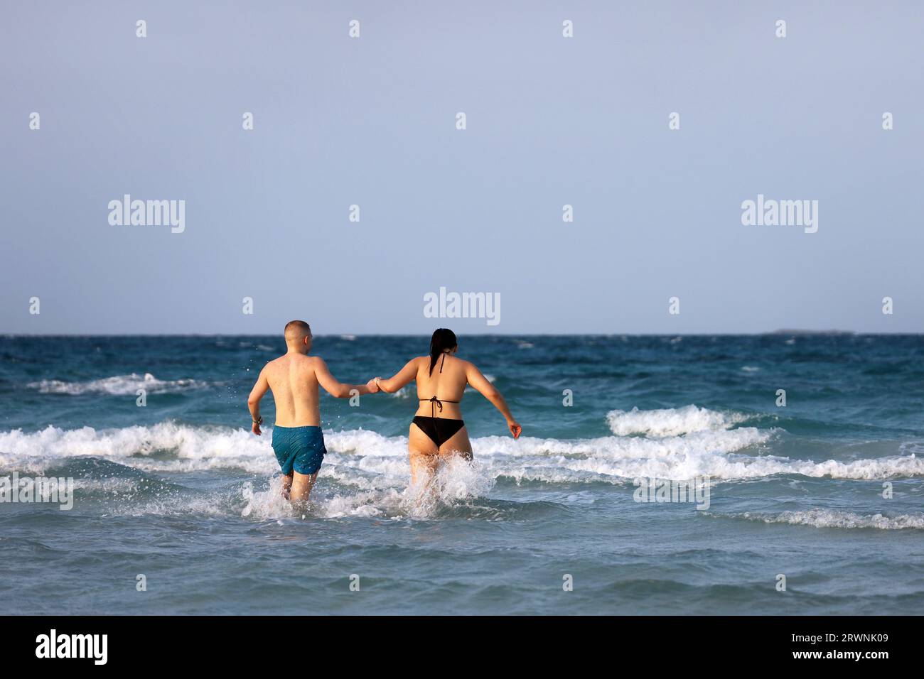 Das Paar läuft in Meereswellen und hält die Hände. Mann und Frau in Wasserspritzern, romantische Freizeit und Strandaktivitäten Stockfoto