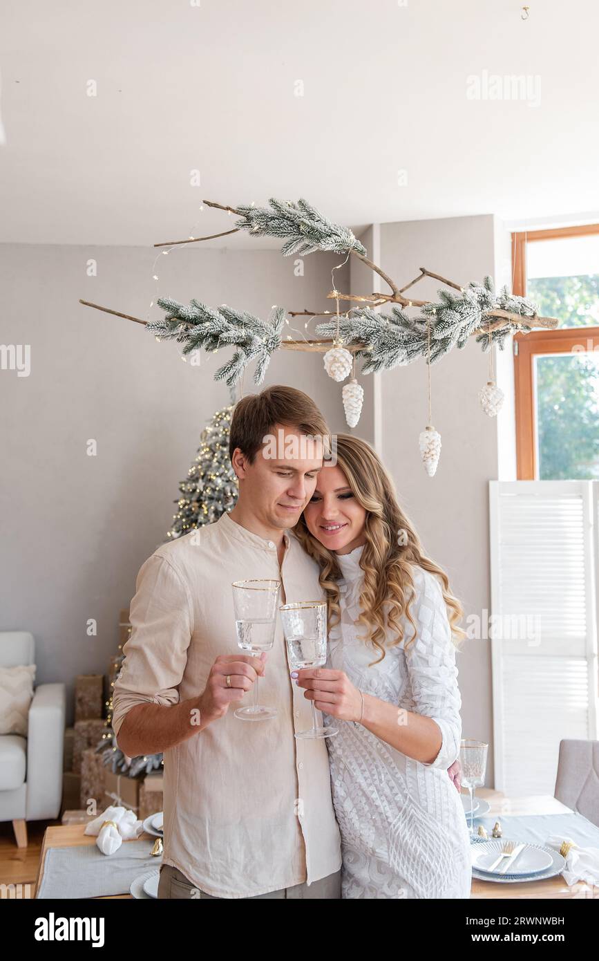 Nahaufnahme eines liebevollen, jungen Modepaares mit einem Glas Champagner zu Weihnachten. Trendige Einrichtung im skandinavischen Stil mit Panoramafenster Stockfoto