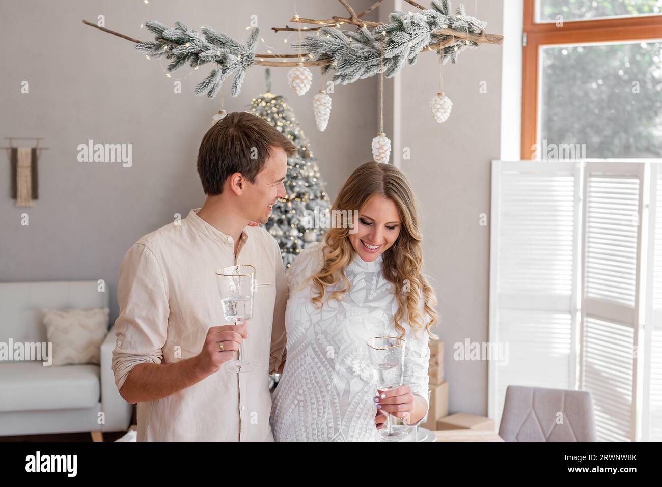 Nahaufnahme eines liebevollen, jungen Modepaares mit einem Glas Champagner zu Weihnachten. Trendige Einrichtung im skandinavischen Stil mit Panoramafenster Stockfoto