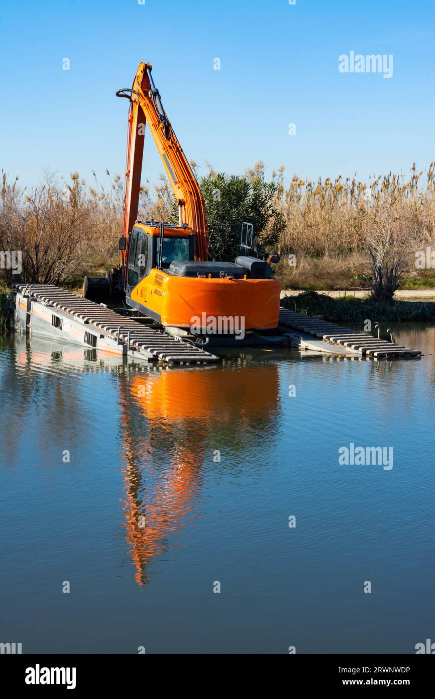 Bagger mit Kette am Ufer eines Kanals oder Baches, der Schlamm aus dem Unterwasser entfernt Stockfoto