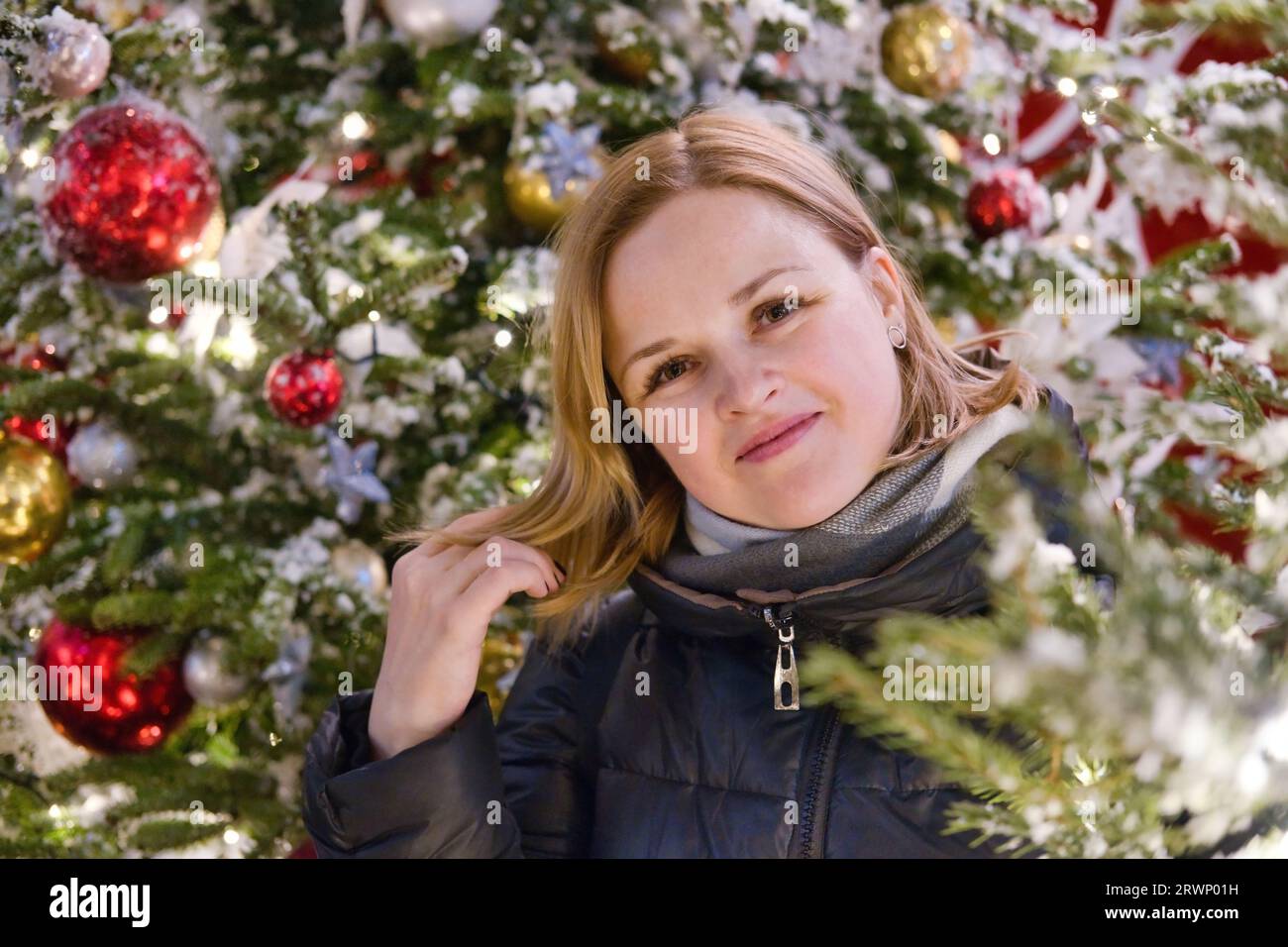 Porträt einer schönen lächelnden europäischen Frau auf Weihnachtsbaumhintergrund. Junge glückliche Frau in den Neujahrsferien. Stockfoto