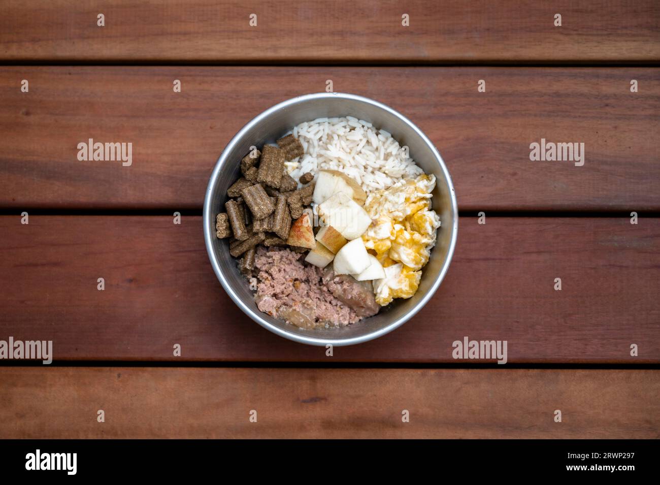 Blick auf eine köstliche hausgemachte Mahlzeit für einen Hund mit Fleisch, Eiern, Apfel, Pellets und Reis. Über Holzbrettern. Stockfoto