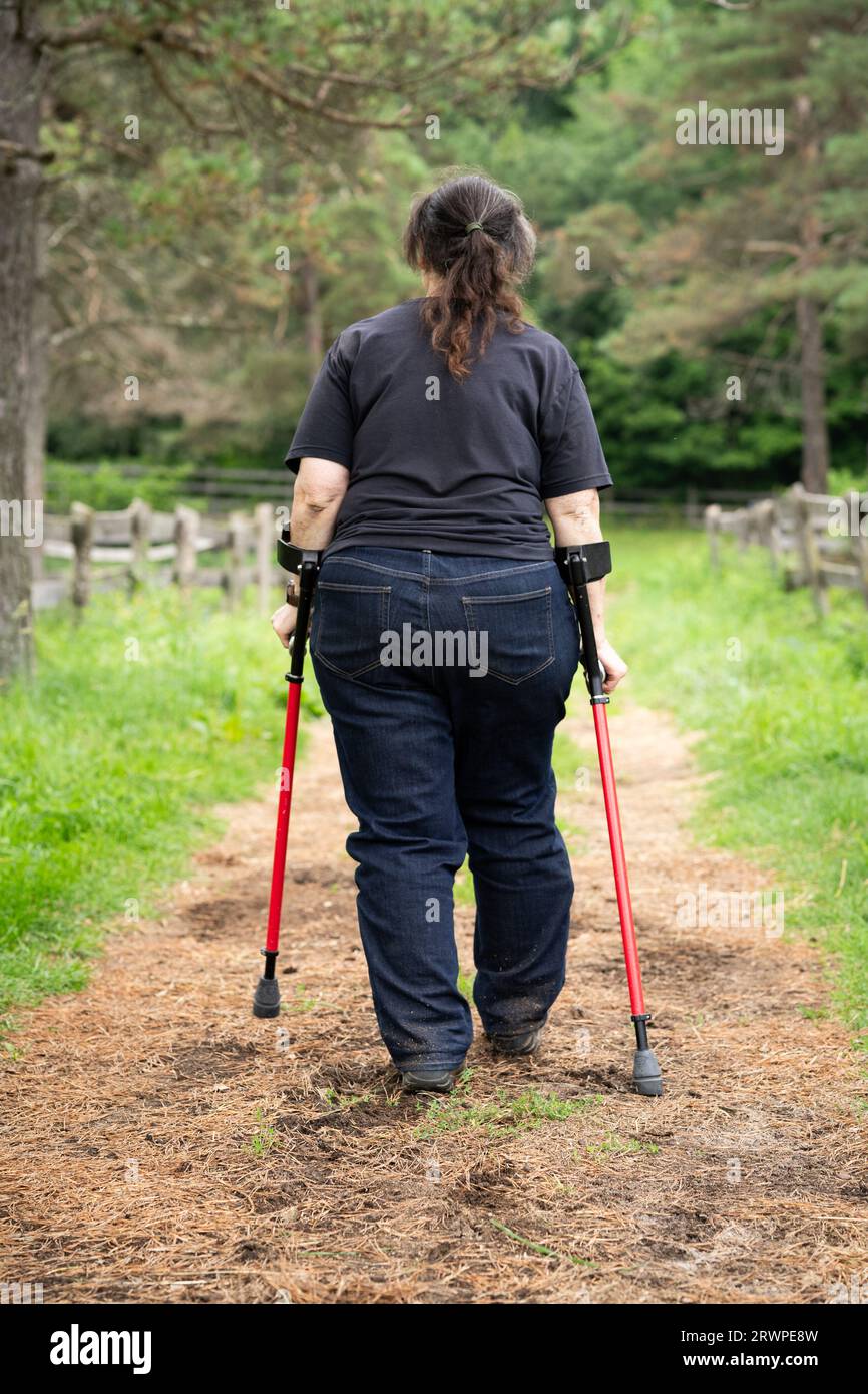 Eine behinderte Frau mit Unterarmkrücken, die auf einem Pfad spaziert Stockfoto