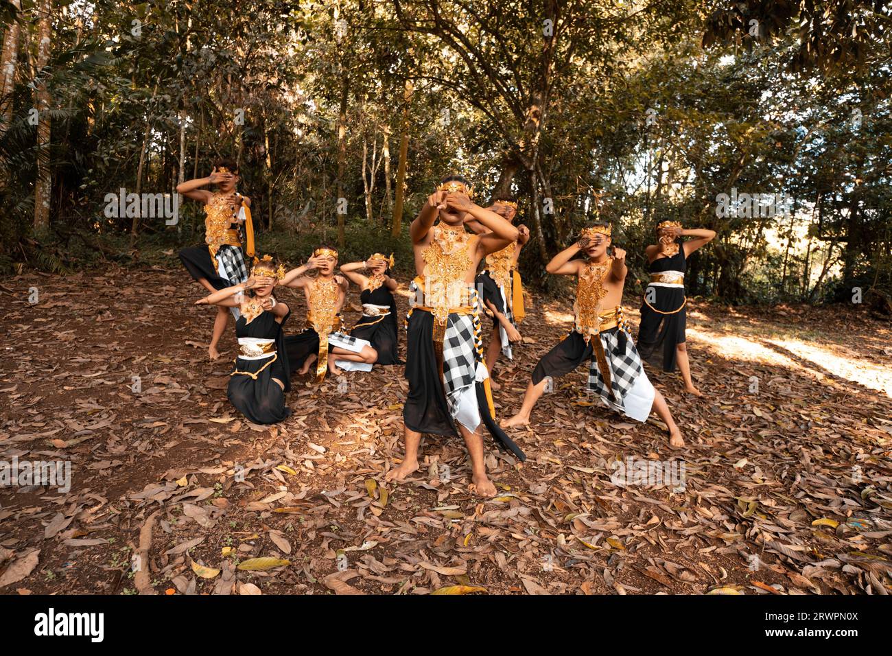 Balinesische Tänzer mit goldenen Kostümen und gestreiften Hosen tanzen zusammen mit den toten braunen Blättern im Hof im Dschungel Stockfoto