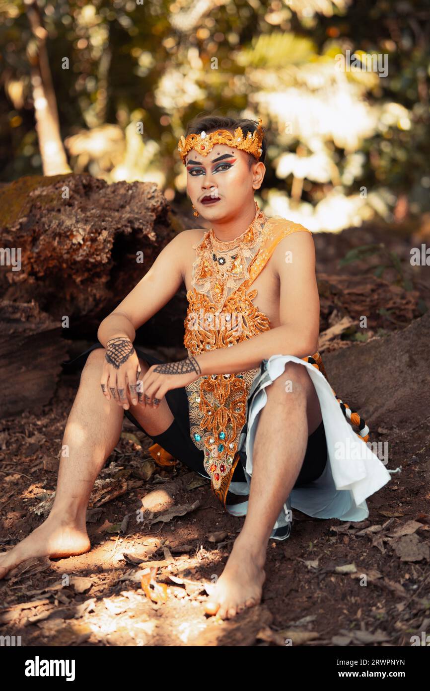 Balinesischer Mann, der im Wald sitzt, während er eine goldene Krone in goldener Kleidung am Tempel trägt Stockfoto