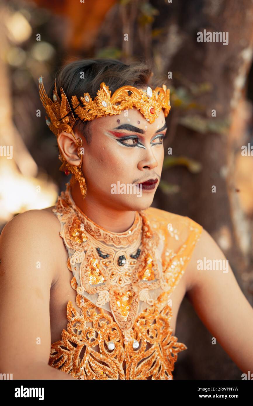 Balinesischer Mann, der im Wald sitzt, während er eine goldene Krone in goldener Kleidung am Tempel trägt Stockfoto