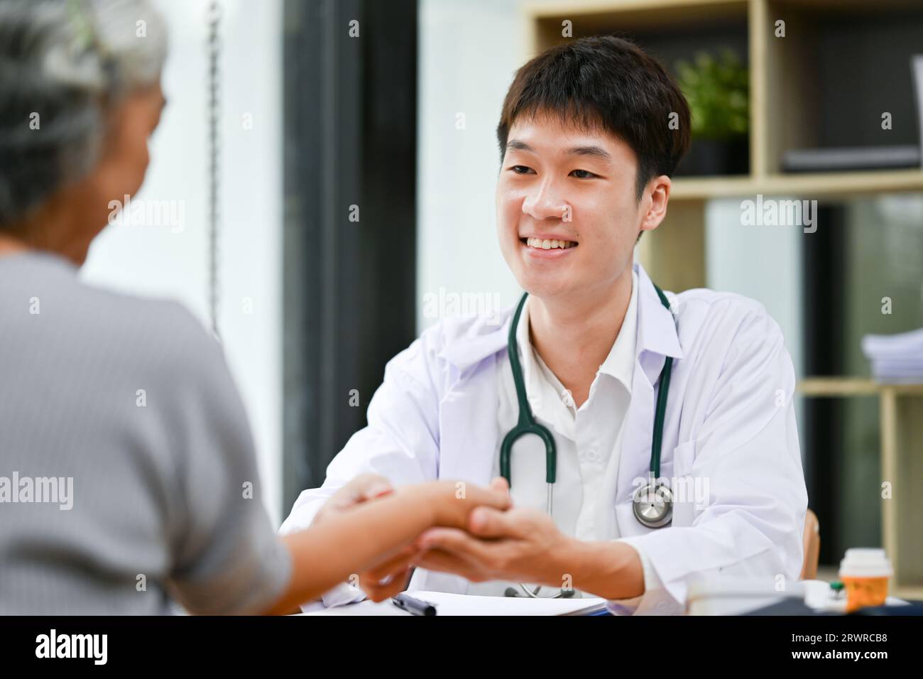 Ein freundlicher und professioneller asiatischer Arzt überprüft den Puls eines Patienten am Handgelenk, während er die Krankheit in seinem Untersuchungsraum diagnostiziert. Medizinisch und h Stockfoto