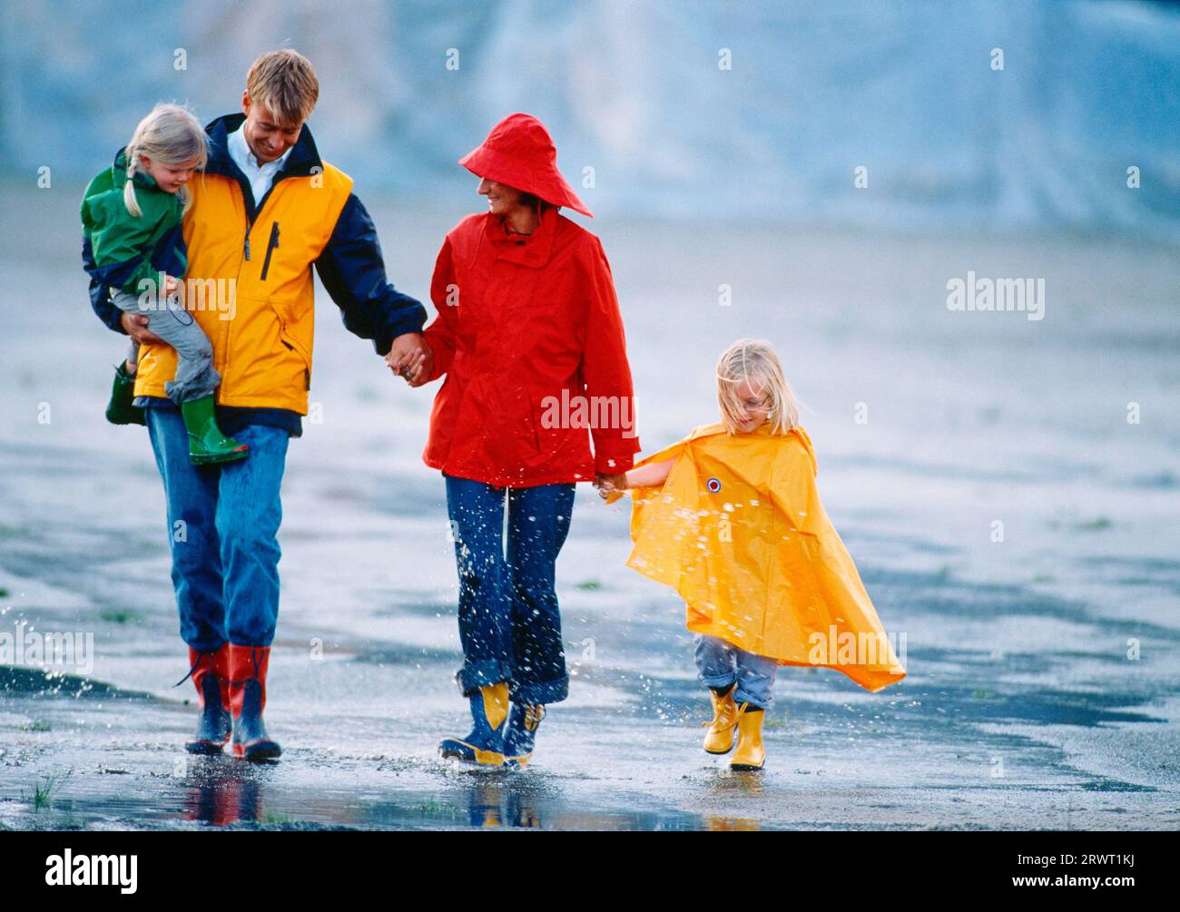 Familie mit 2 Kindern in farbenfroher Regenkleidung auf einer digitalen und KB-Rutsche Stockfoto