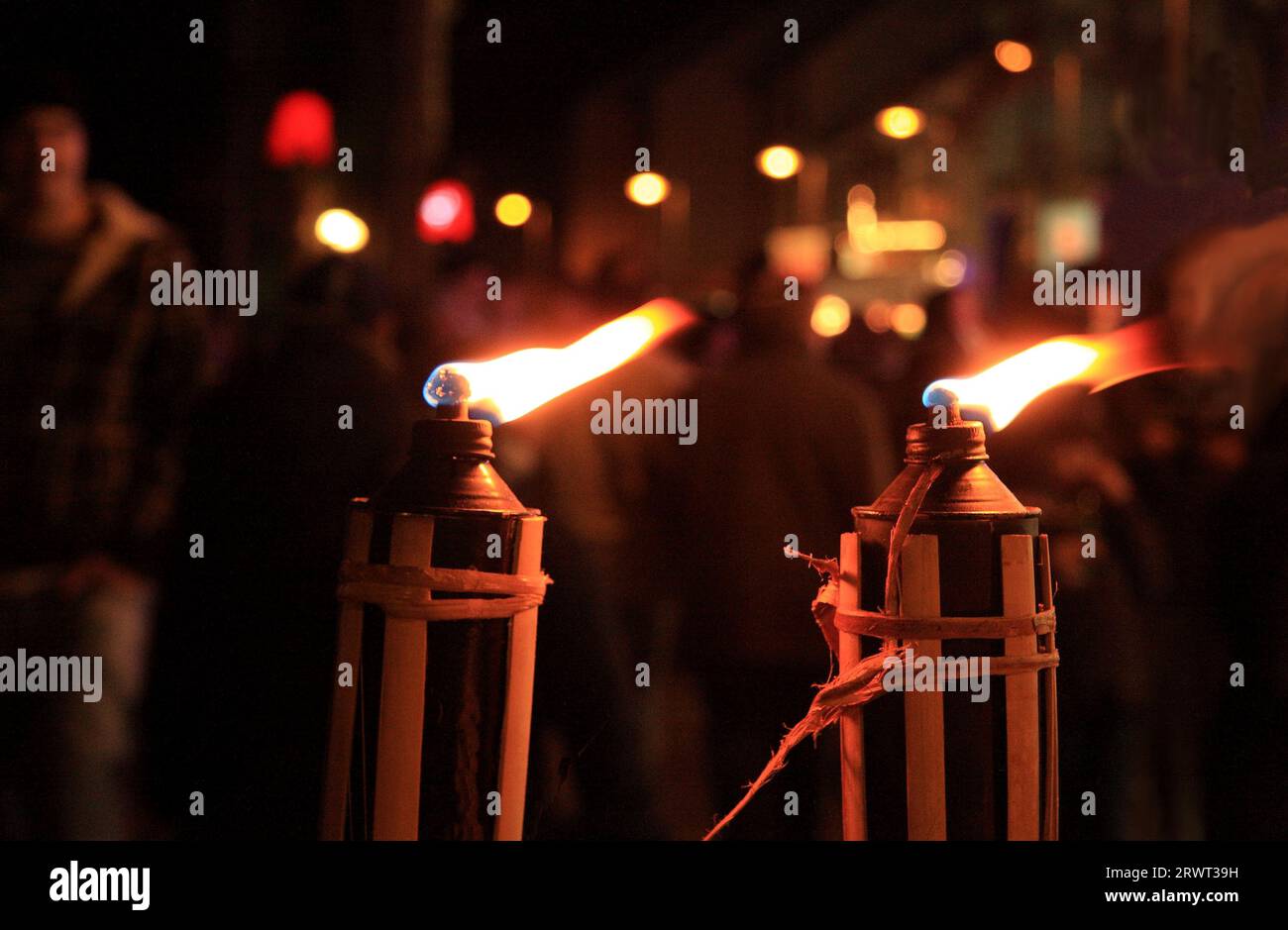 Zwei brennende Fackeln, unscharfe Hintergrundperson und bunte Lichter Stockfoto