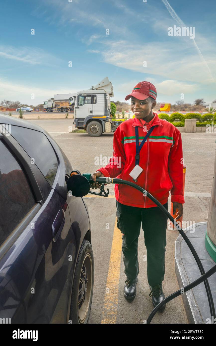 afroamerikaner in Uniform an der Tankstelle, ein kleines Auto mit Benzin befüllt, Düse im Tank Stockfoto