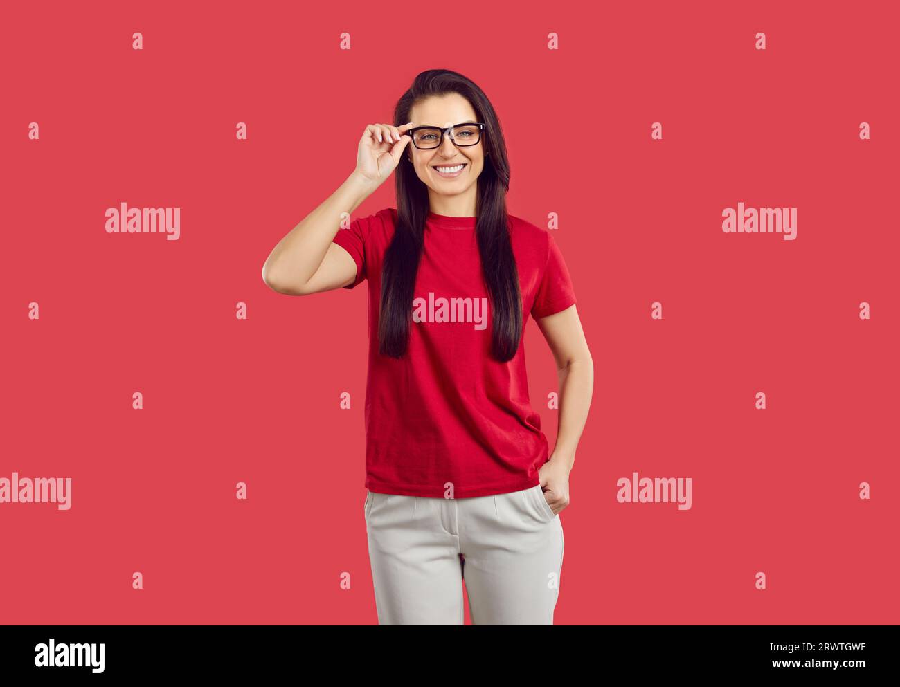 Porträt der glücklichen jungen Frau in schwarzer klassischer Brille isoliert auf rotem Hintergrund. Stockfoto