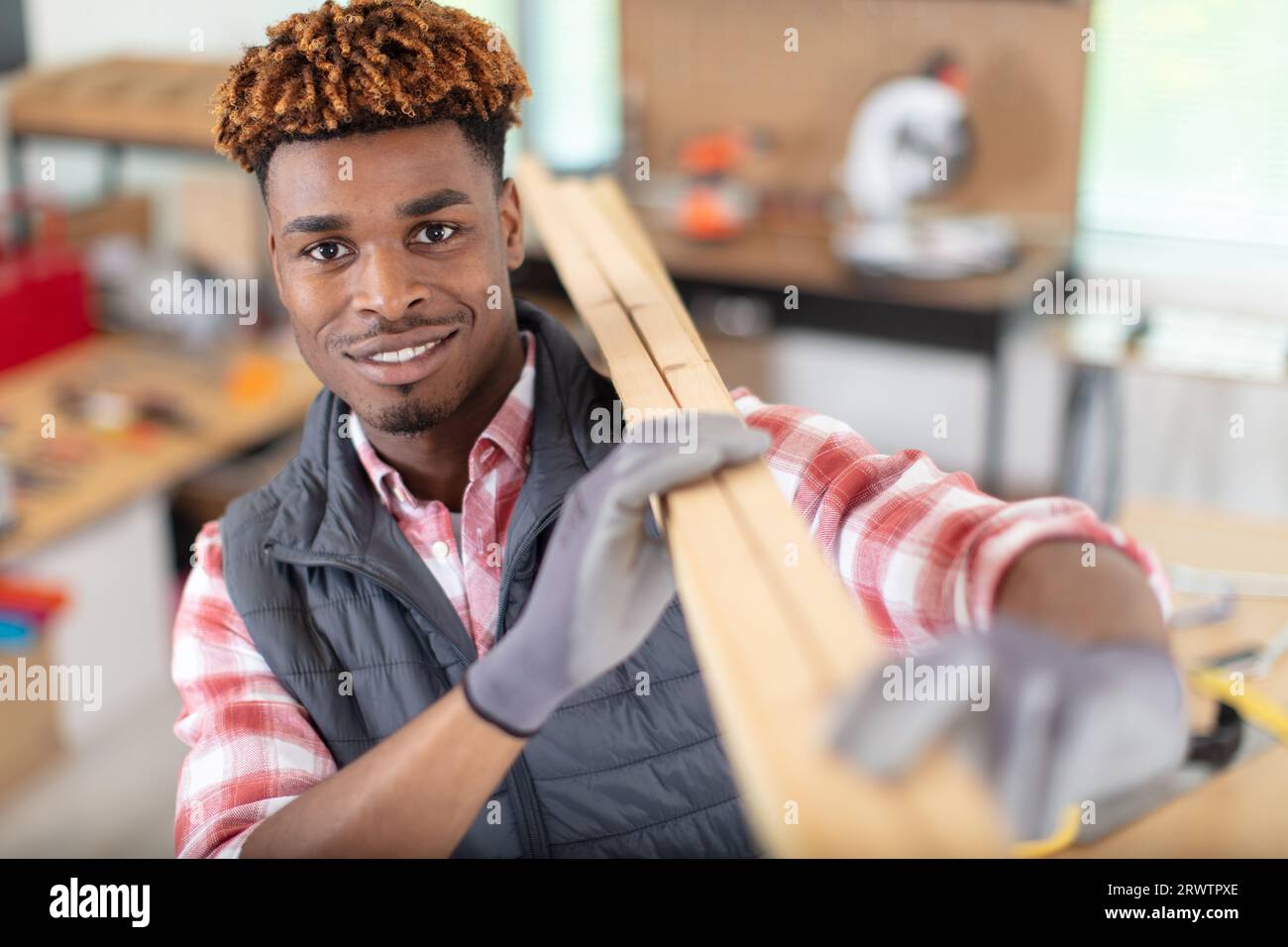 Junger Mann in Handschuhen mit Holzbrettern auf der Schulter Stockfoto