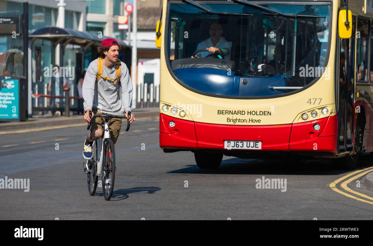 Junger Mann, der ohne Helm auf dem Fahrrad fährt. Männlicher Radfahrer, der in Großbritannien auf einer Straße um einen Bus fährt, ohne einen Fahrradhelm zu tragen. Stockfoto