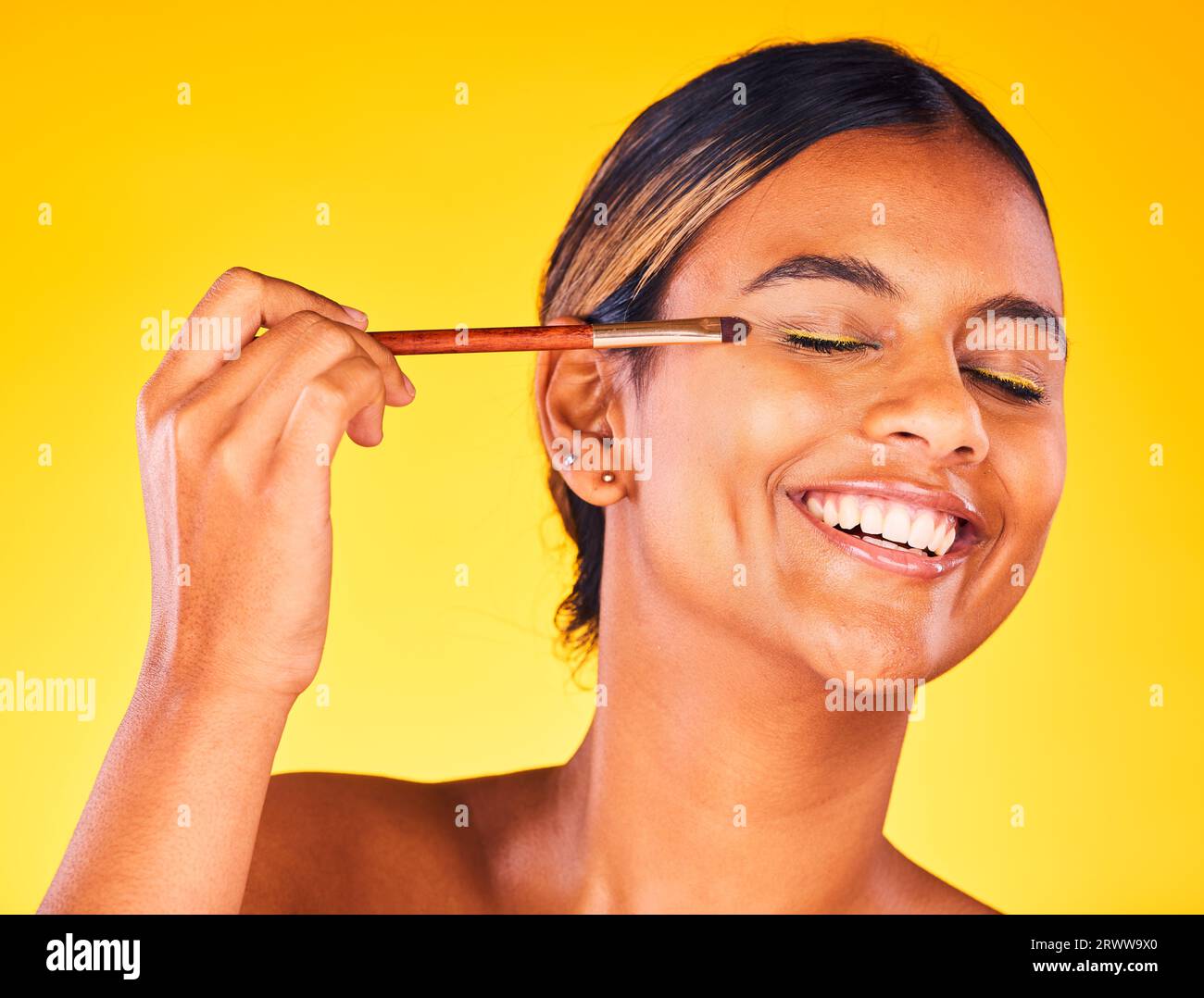 Frau, Augen-Make-up und Schönheit mit Gesicht, Bürste für Kosmetik und kosmetisches Produkt auf gelbem Hintergrund. Glückliches Modell, Puder oder Foundation mit auftragen Stockfoto