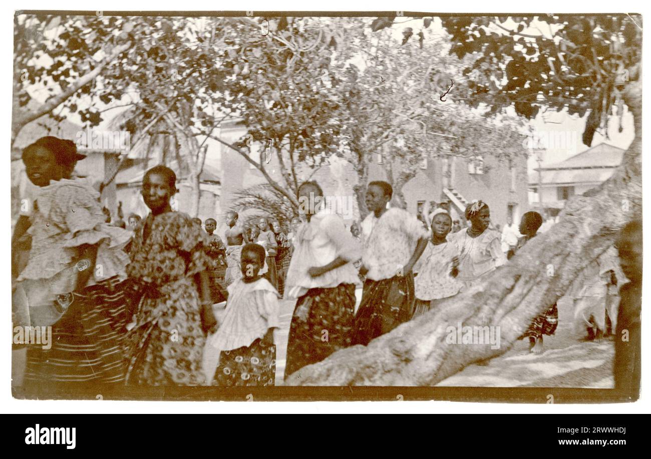 Zwei lange Linien von Frauen verlaufen entlang einer Straße, die von Bäumen und Gebäuden gesäumt ist. Die Bildunterschrift eines Begleitbildes beschreibt das Ereignis als Karfreitagsprozession in Winneba. Stockfoto