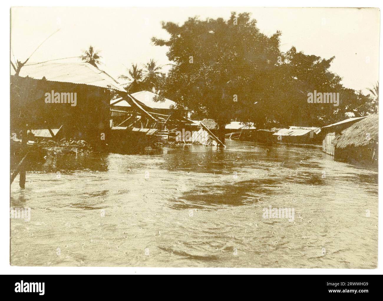 Schauplatz einer Überschwemmung, mit Bäumen und Holz- und Strohhäusern, die aus dem Wasser ragen. Einige der Strukturen sind zusammengebrochen. Stockfoto