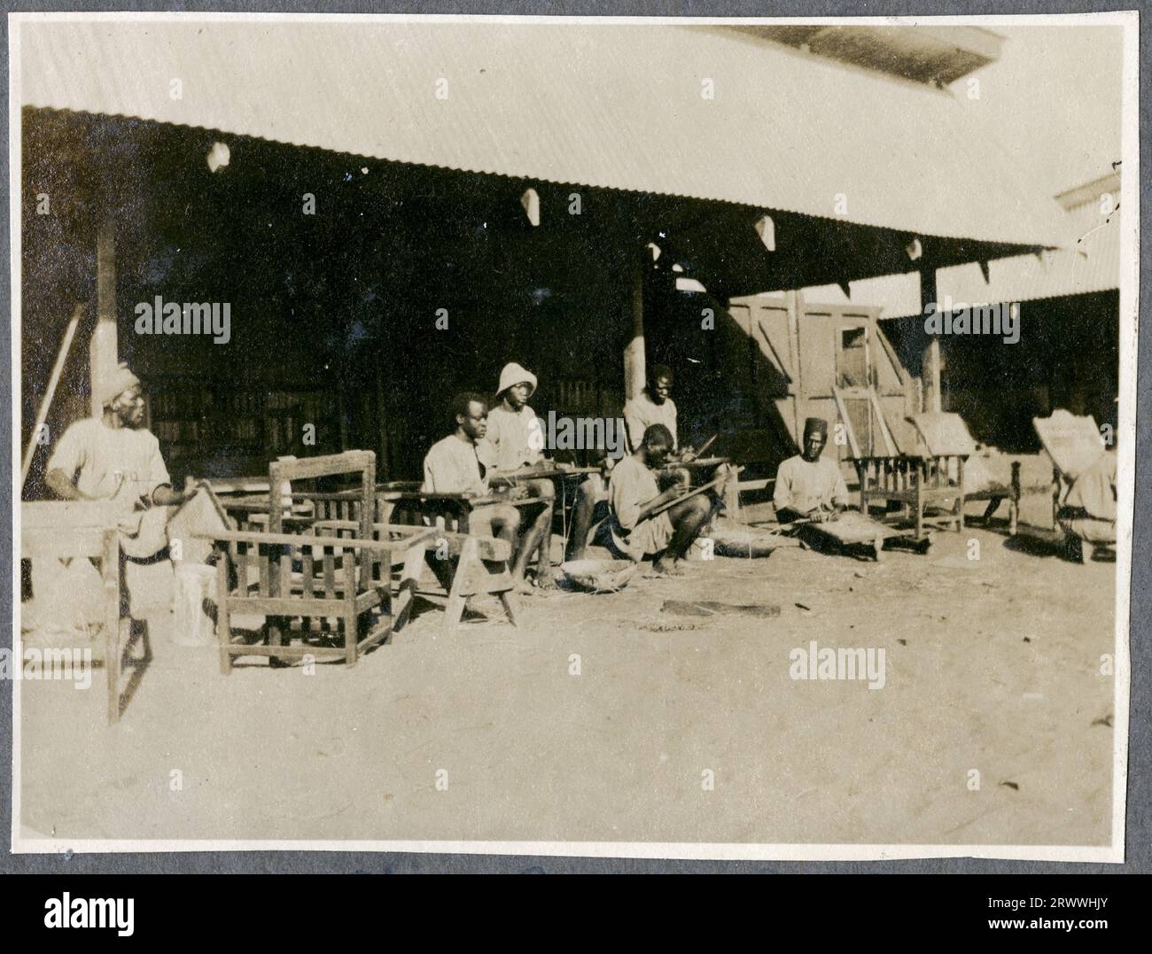 Gruppe von Lehrlingen der Abteilung für öffentliche Arbeiten, die bei Sonnenschein auf Rohrstühlen arbeiten. Originalhandschrift: Chair Caning P.W.D. Stockfoto