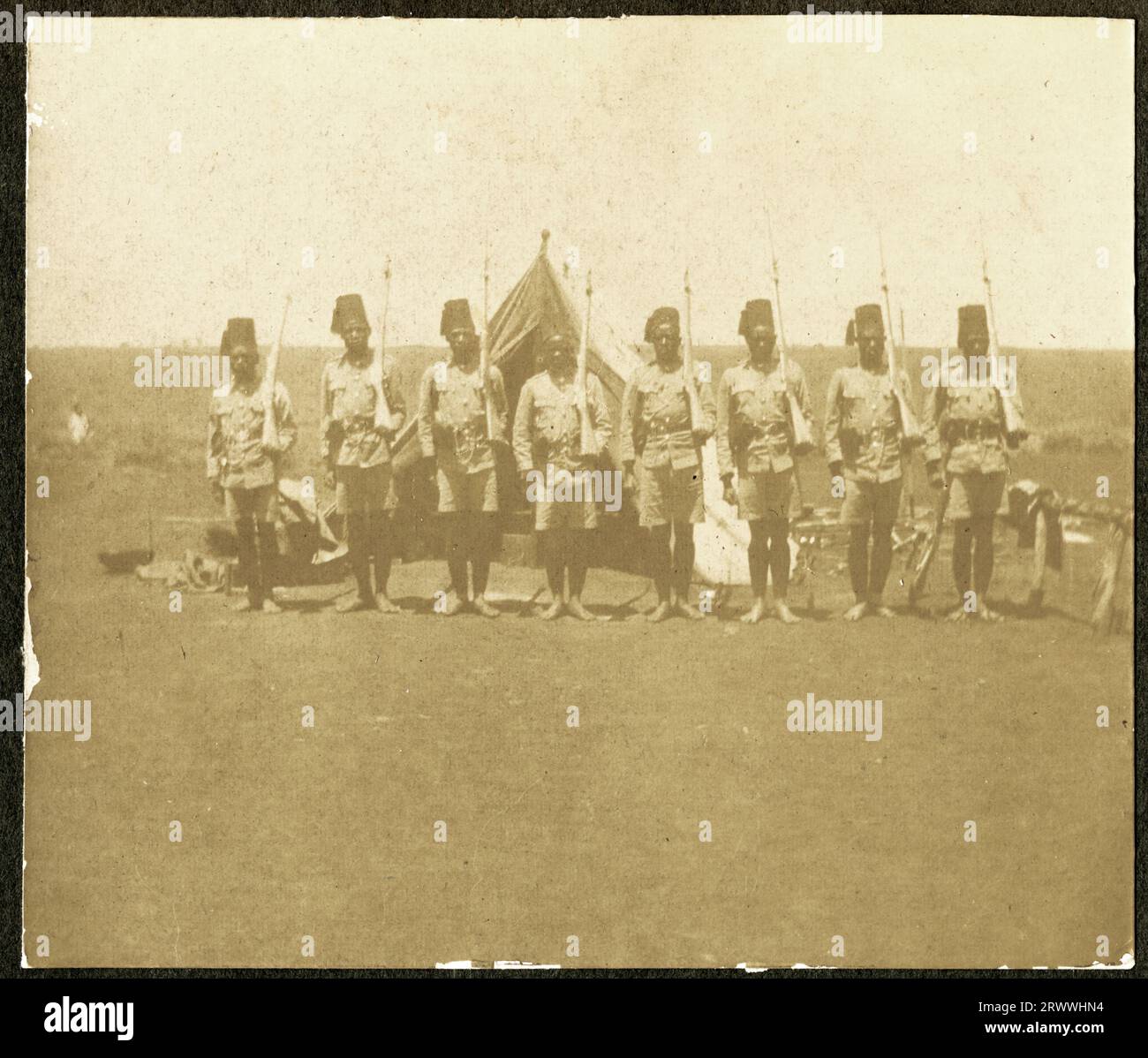 Einer von vier Drucken zeigt King's African Rifles Soldaten, die Nairobi verlassen, um in Deutsch-Ostafrika (Tansania) zu kämpfen. Dieser Druck zeigt eine Kolumne europäischer Offiziere und afrikanischer Askari auf einer Waldlichtung, die von links nach rechts marschiert und auf der rechten Seite des Bildes eine Blaskapelle spielt. Ursprünglicher Seitentitel: Abfahrt. 1/2nd Bn: K.A.R. 4. August 1916. Stockfoto