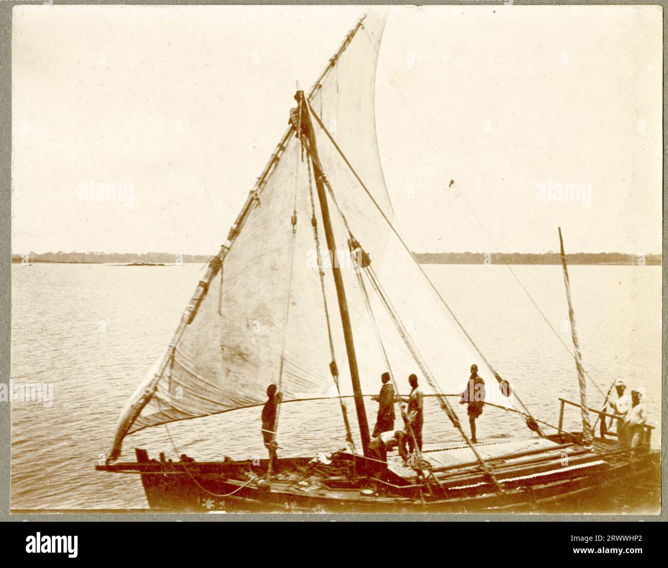Drei afrikanische Männer, die Tierhäute um die Schultern tragen, paddeln auf einem Kanu durch das Schilf am Rande des Viktoriasees. Das Kanu hat einen langen Stachel, der vorne hervorsteht. Originaltitel des Manuskripts: Kanu. Auf Victoria Nyanza. Stockfoto