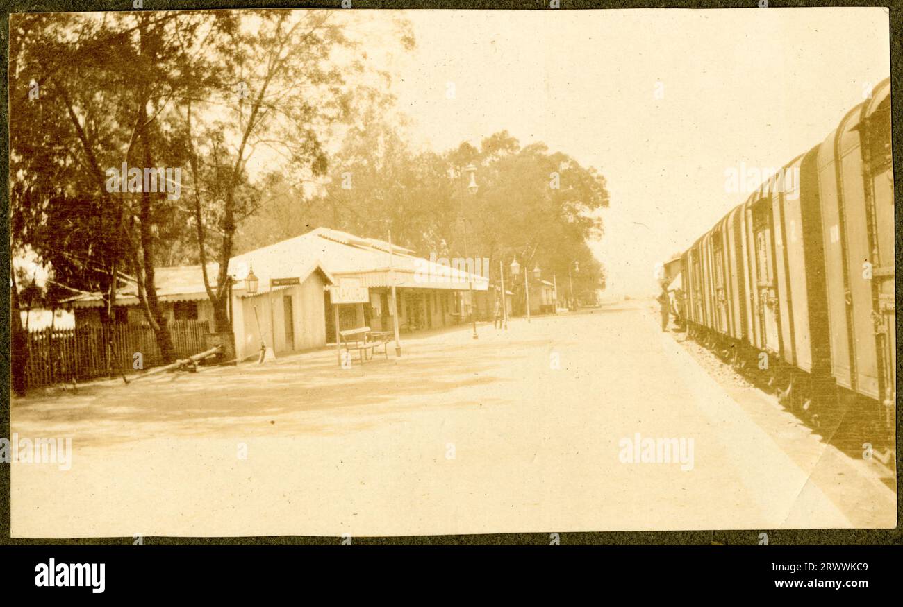 Sehen Sie den Bahnsteig am Bahnhof Nakuru hinunter, mit einer Sammlung von Bahnhofsgebäuden und Lampen auf der linken Seite und einem stationären Zug der Uganda Railway auf der rechten Seite. Originaltitel des Manuskripts: Nakuru Station. Stockfoto