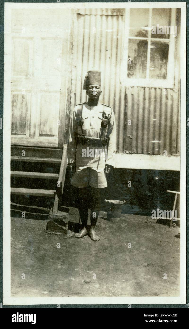 Porträt eines afrikanischen Soldaten in K.A.R.-Uniform, der vor einem Wellblechgebäude steht. Originalhandschrift: R.S.M. Juma 2. K.A.R. Stockfoto