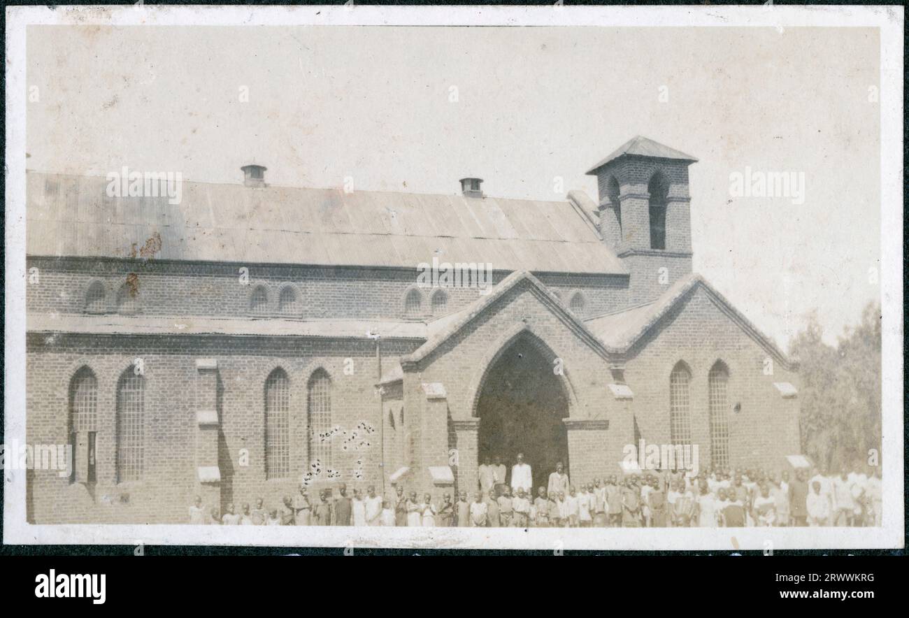 Blick auf eine große Kirche mit Dutzenden afrikanischer Kinder vor ihren Mauern. In der Tür sind eine kleine Anzahl von Erwachsenen. Originalhandschrift: Eine Heimatschule in Zomba C.A. Stockfoto