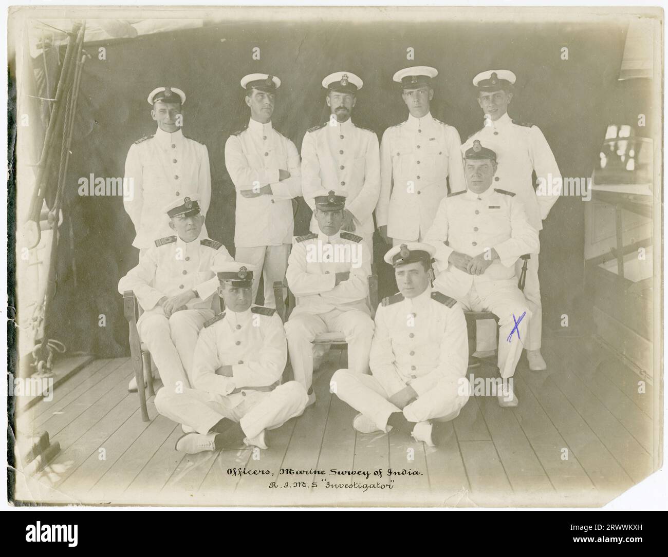 Porträtfoto, aufgenommen auf einem Schiff, einer Gruppe uniformierter Schiffsoffiziere, identifiziert in gedruckter Beschriftung am unteren Rand des Fotos als Offiziere des Marine Survey of India. Der Name des Schiffes ist R.I.M.S. Investigator. George EllisWood (R.I.M.) ist durch ein X auf der rechten Seite des Fotos gekennzeichnet. Die Beschriftung auf der Rückseite lautet: G E HOLZFELGE ca. 1916-20. Stockfoto