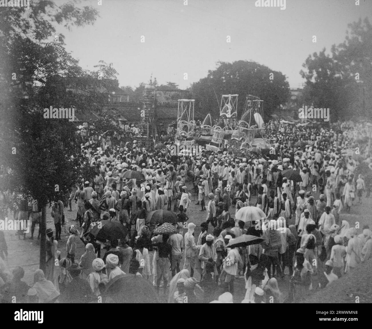 Religiöse Prozession mit geschmückten Wagen inmitten eines großen Festes von traditionell gekleideten Indianern. Bäume säumen den Platz und Gebäude sind im Hintergrund zu sehen. Stockfoto