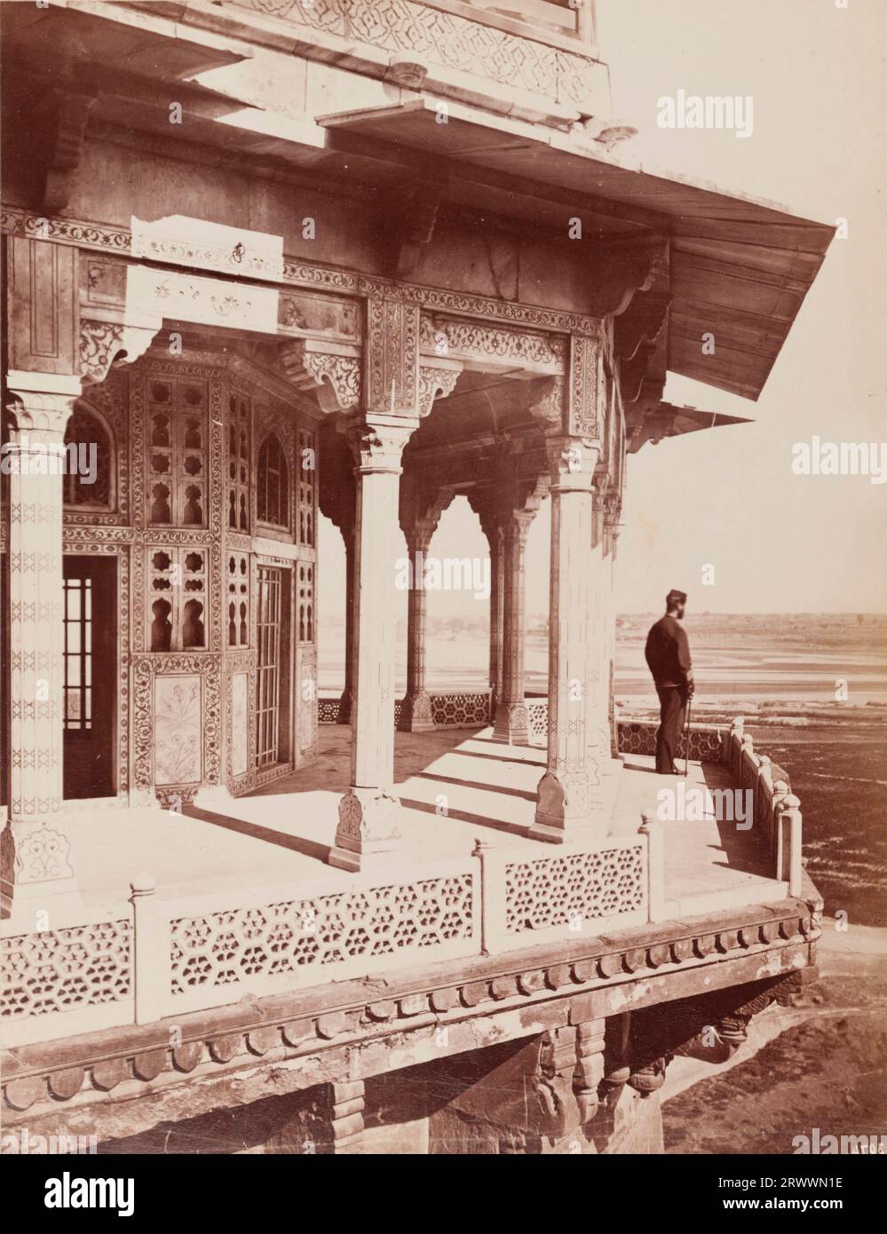 Eine Einzelperson blickt von einem Balkon auf den Samman Burj, einen achteckigen Turm, der in der Nähe der Diwan-e-Khas-Halle des Shah Jahan steht und sich im Agra Fort Komplex befindet. Die islamische Architektur ist kunstvoll im traditionellen Mogulstil dekoriert, mit organischen Motiven und geometrischem Design. Die Bildunterschrift lautet: Blick von den Wänden, Agra. Stockfoto