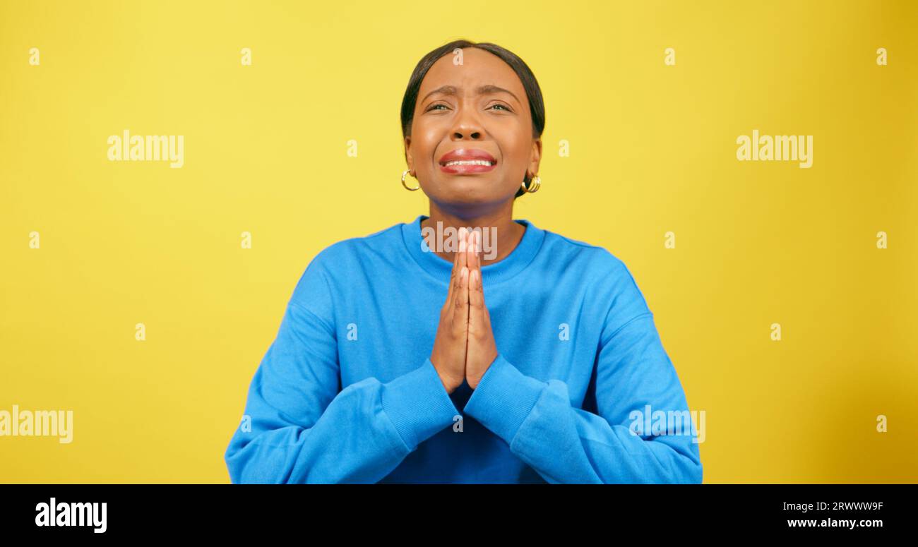 Emotionale junge Frau betet und bittet, bettelnd und verärgert, gelbes Studio Stockfoto